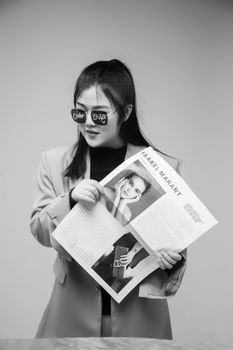 A fashionable woman in sunglasses poses with a magazine in black and white.