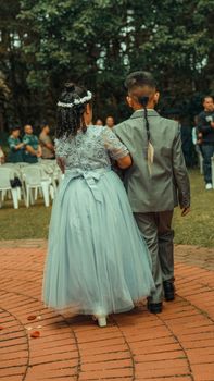 A boy and girl in formal wear walking together at an outdoor wedding ceremony.