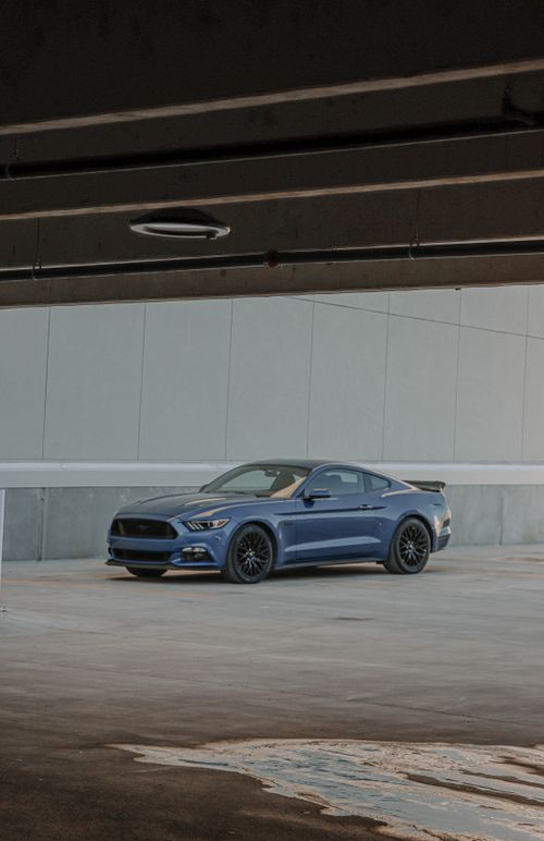 Free A blue Ford Mustang parked in a modern urban environment under a concrete structure. Stock Photo