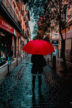 A person with a red umbrella walking on a rainy street in Madrid, Spain.