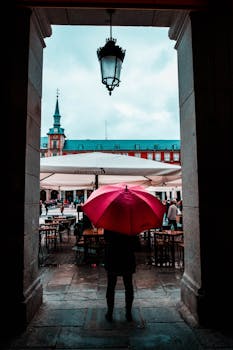 A person with a red umbrella in Plaza Mayor, Madrid, on a rainy day.