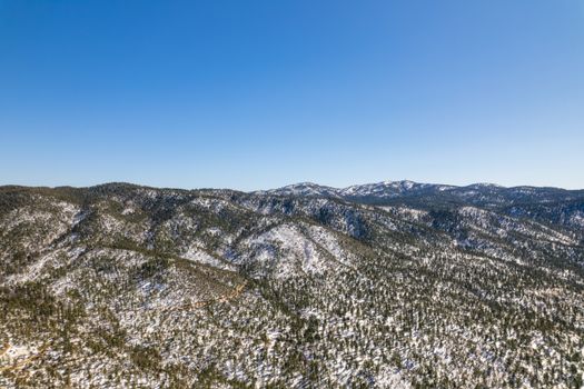 Drone shot of a scenic snow-covered mountain range under a clear blue sky.