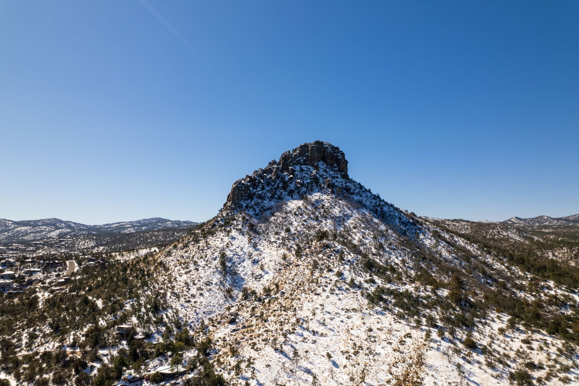 Aerial view of Thumb Butte mountain covered in snow against a clear blue sky in Prescott, Arizona.