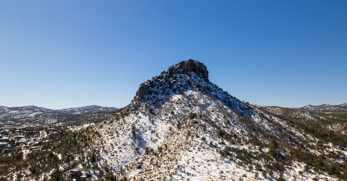 Aerial view of Thumb Butte mountain covered in snow against a clear blue sky in Prescott, Arizona.