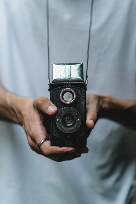 Close-up of hands holding a vintage camera outdoors in a casual setting.
