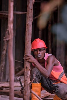 African man in safety helmet and gear at construction site holding tools.