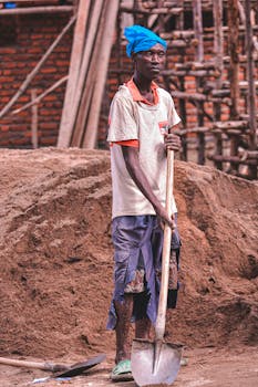 African construction worker holding a shovel at an outdoor site.