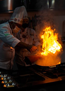 Chefs add flair with a blazing flambé technique in a modern kitchen setting. Perfect for culinary enthusiasts.