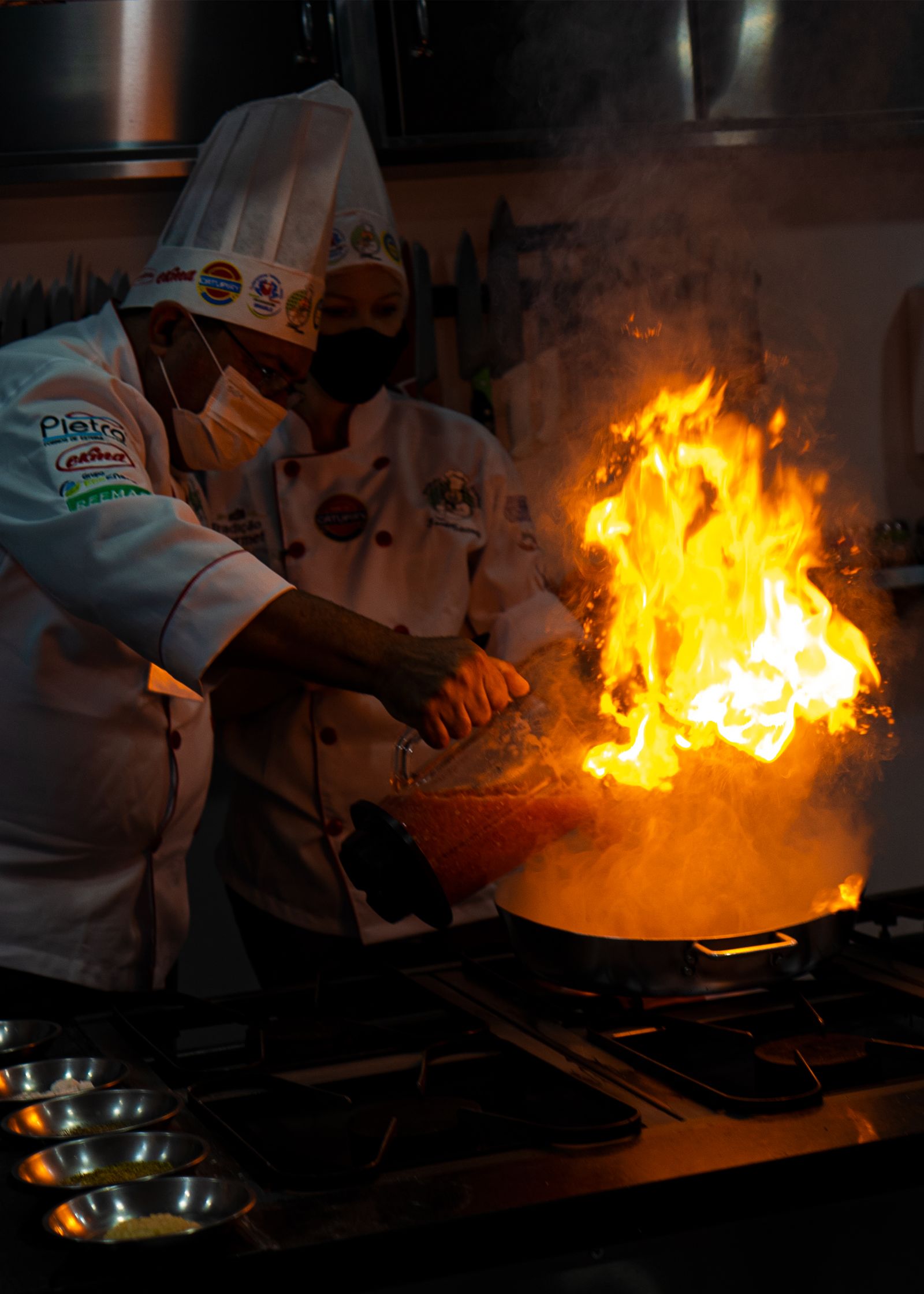 Chefs creating a blazing flambé over a pan in a modern kitchen