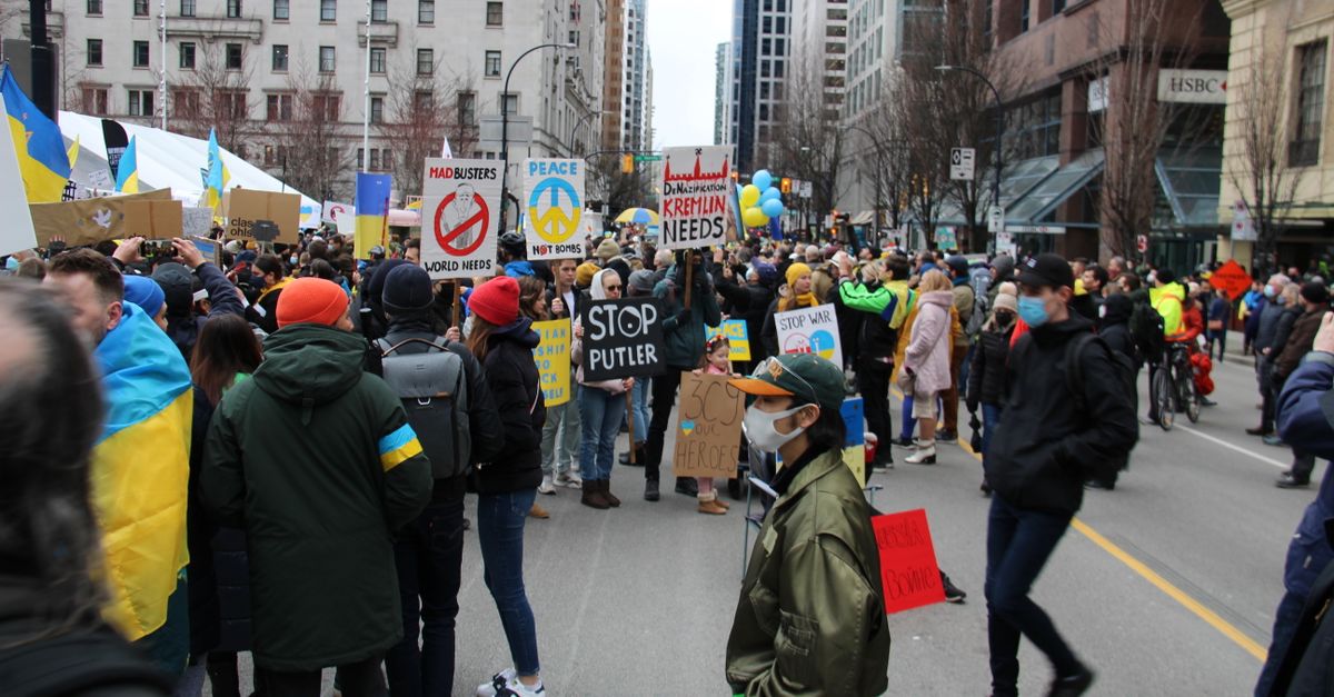 Demonstrators with signs and flags gather for activism in downtown Vancouver, promoting peace and global unity.