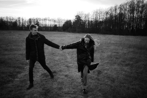 Free A couple walking hand in hand through a grassy field in black and white, exuding romance. Stock Photo