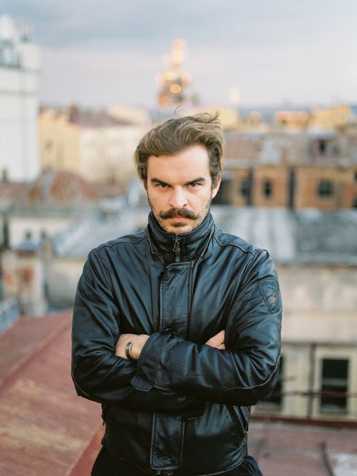 Free Portrait of a man with a moustache in a leather jacket standing on an urban rooftop with a moody expression. Stock Photo