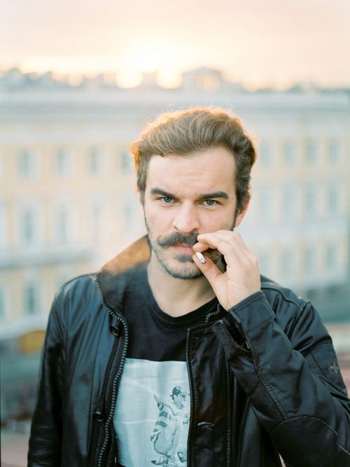 Free A stylish man smokes a cigarette outdoors, wearing a black leather jacket in an urban setting. Stock Photo