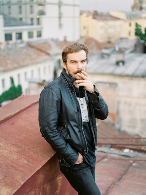 A Man in a Leather Jacket Smoking a Cigarette on the Rooftop
