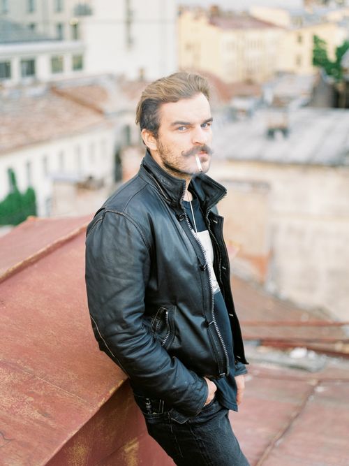 Free Stylish man with a mustache in a black leather jacket smoking on a rooftop. Stock Photo