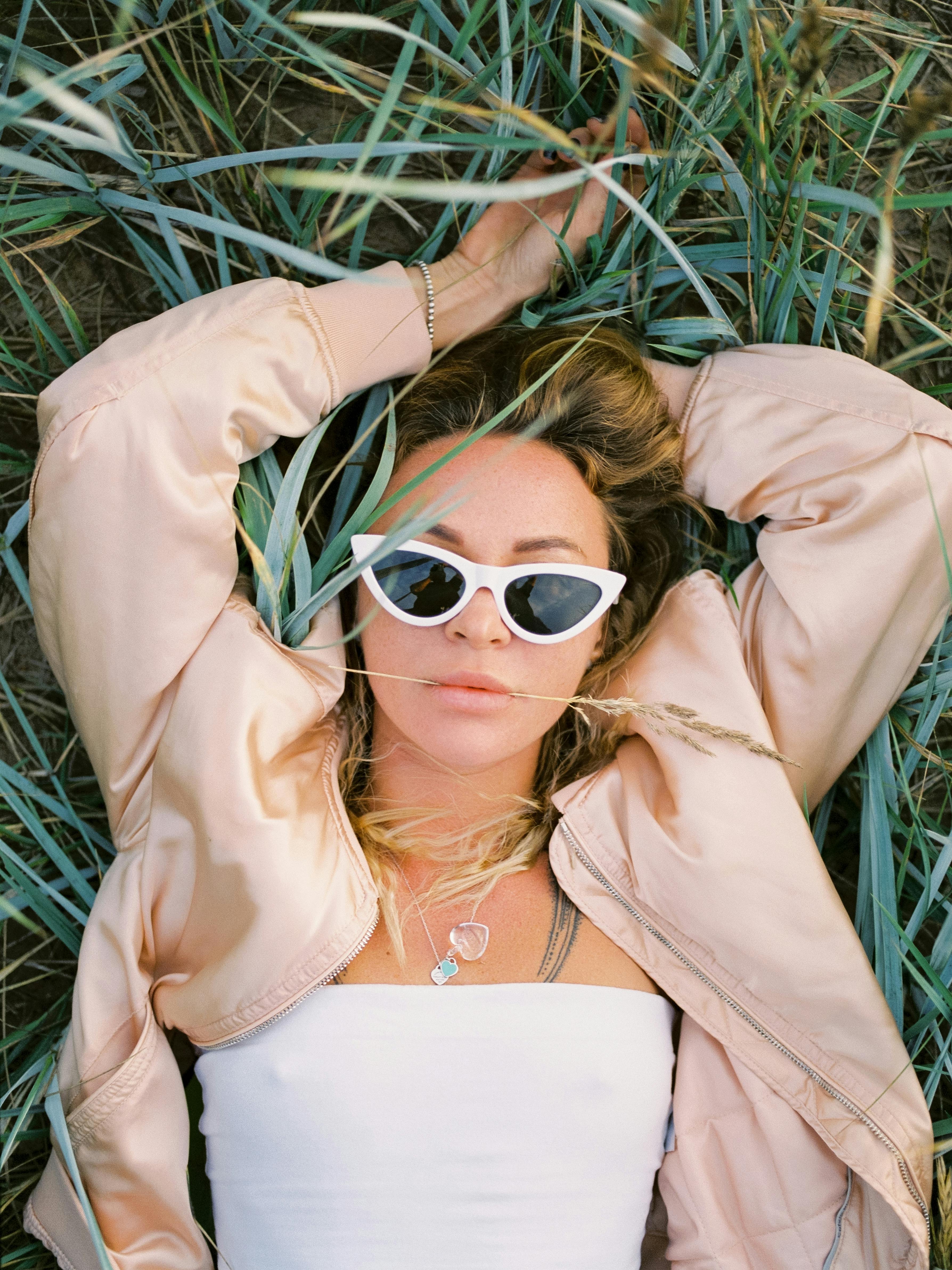 Relaxed woman with sunglasses lying on grass, embodying summer vibes.