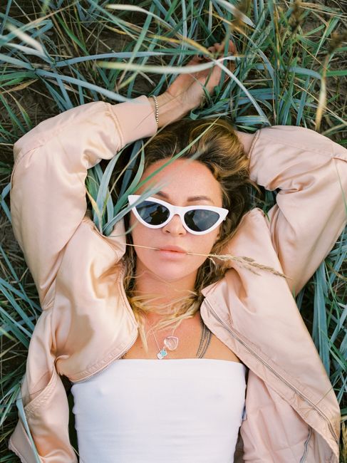 Relaxed woman with sunglasses lying on grass, embodying summer vibes.