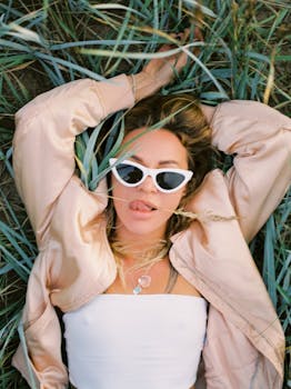 Relaxed woman in sunglasses and jacket lying in grass, exuding a carefree vibe.