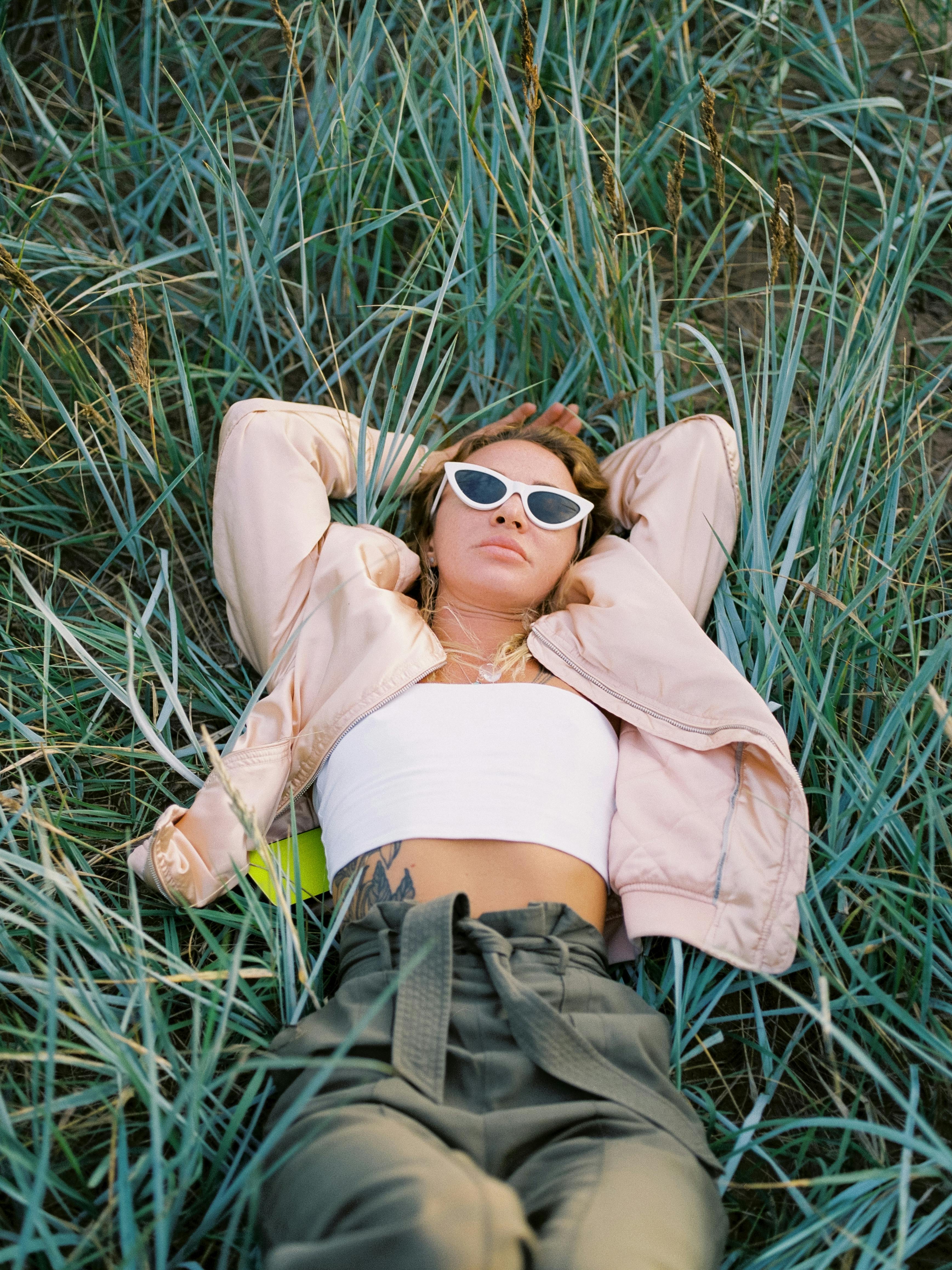 A woman in trendy sunglasses relaxes in the grass, reflecting a modern lifestyle.