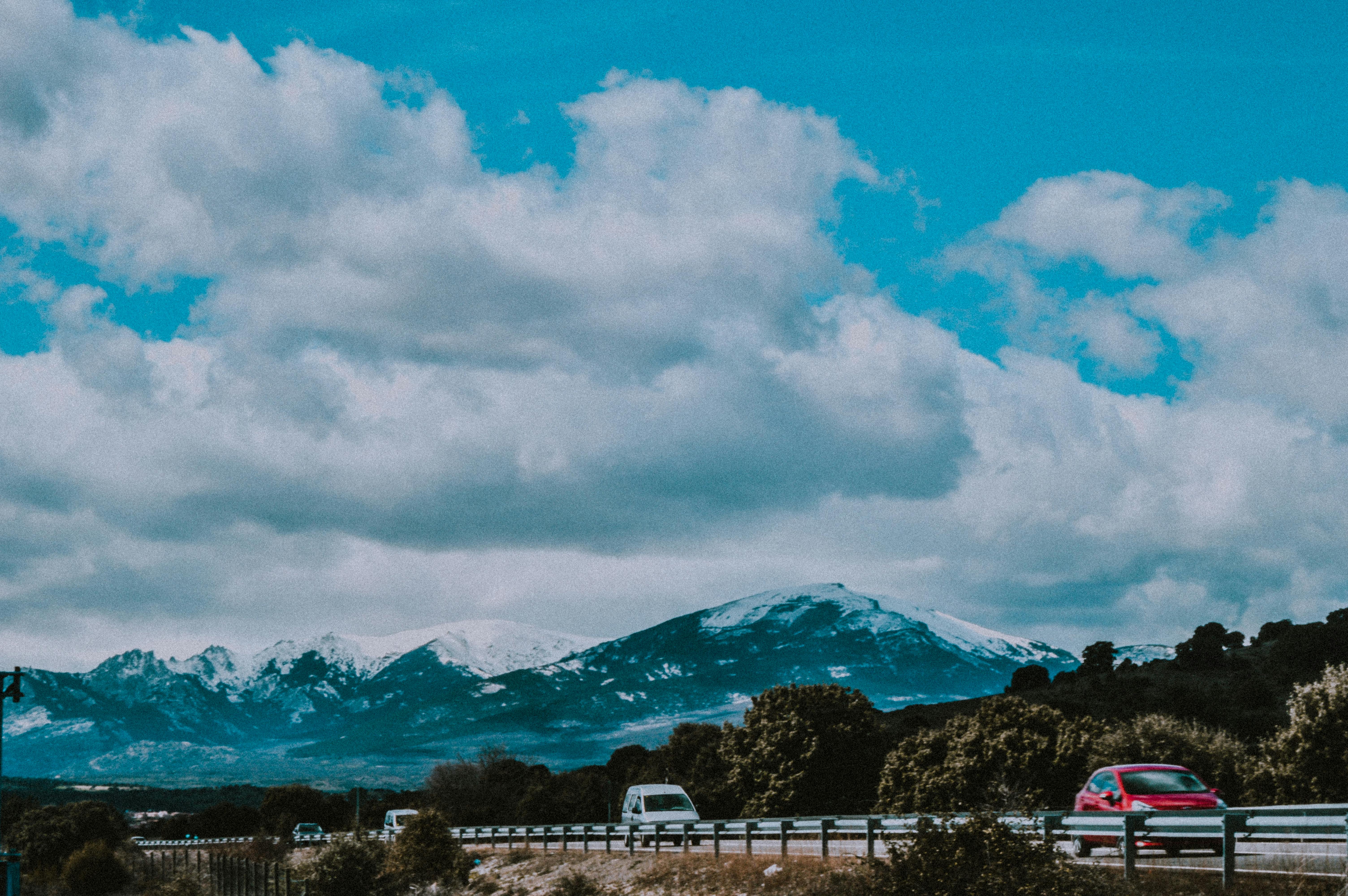 在西班牙马德里，一辆汽车行驶在风景优美的道路上，山上白雪皑皑，天空多云