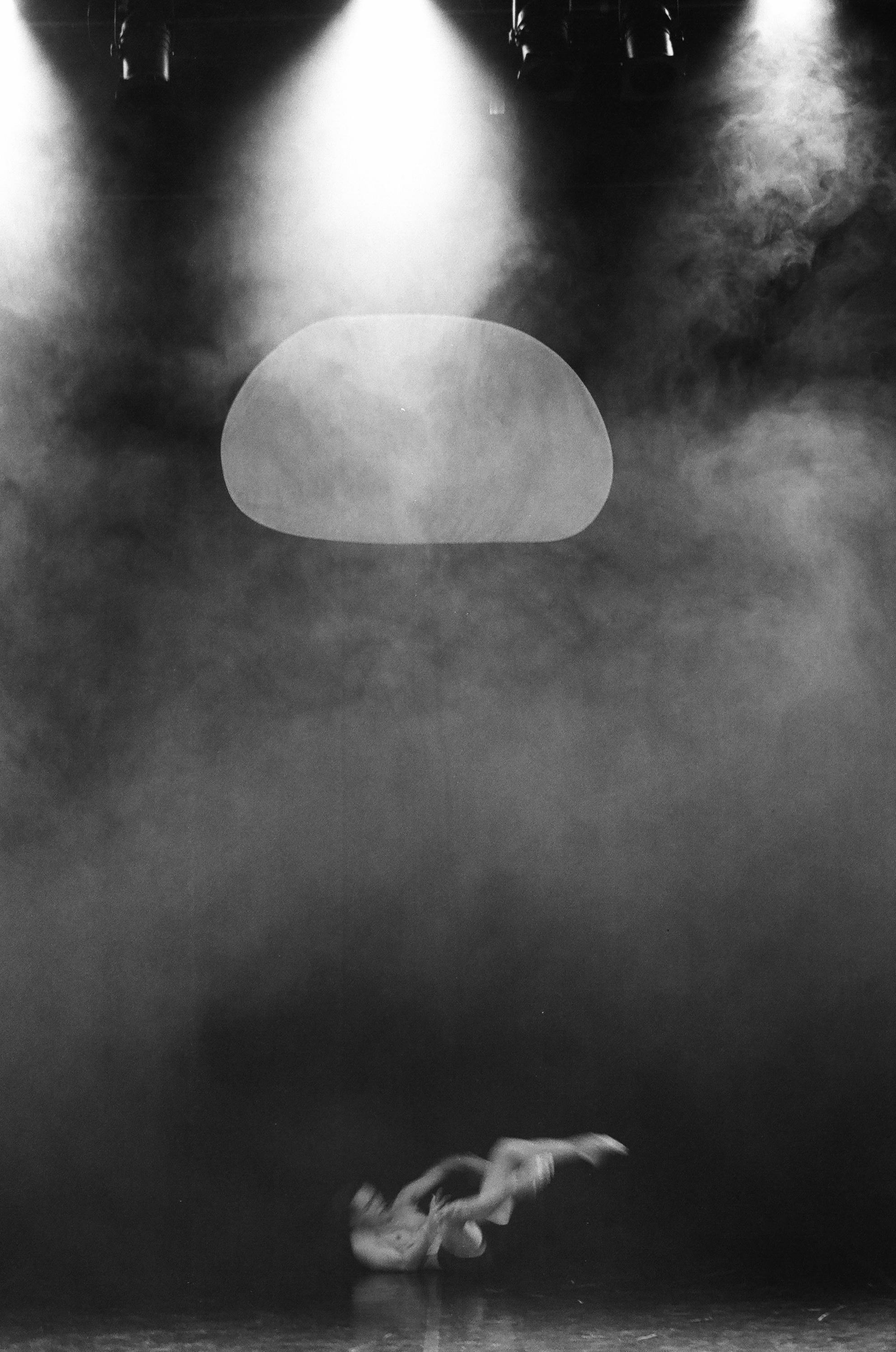 Artistic black and white photo of a dynamic dance performance on stage with dramatic lighting and smoke.