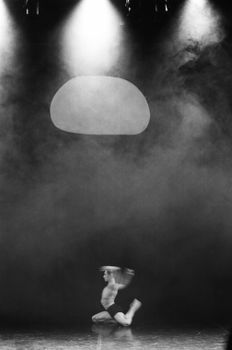 Artistic black and white photo of a shirtless dancer performing on a smoky stage.