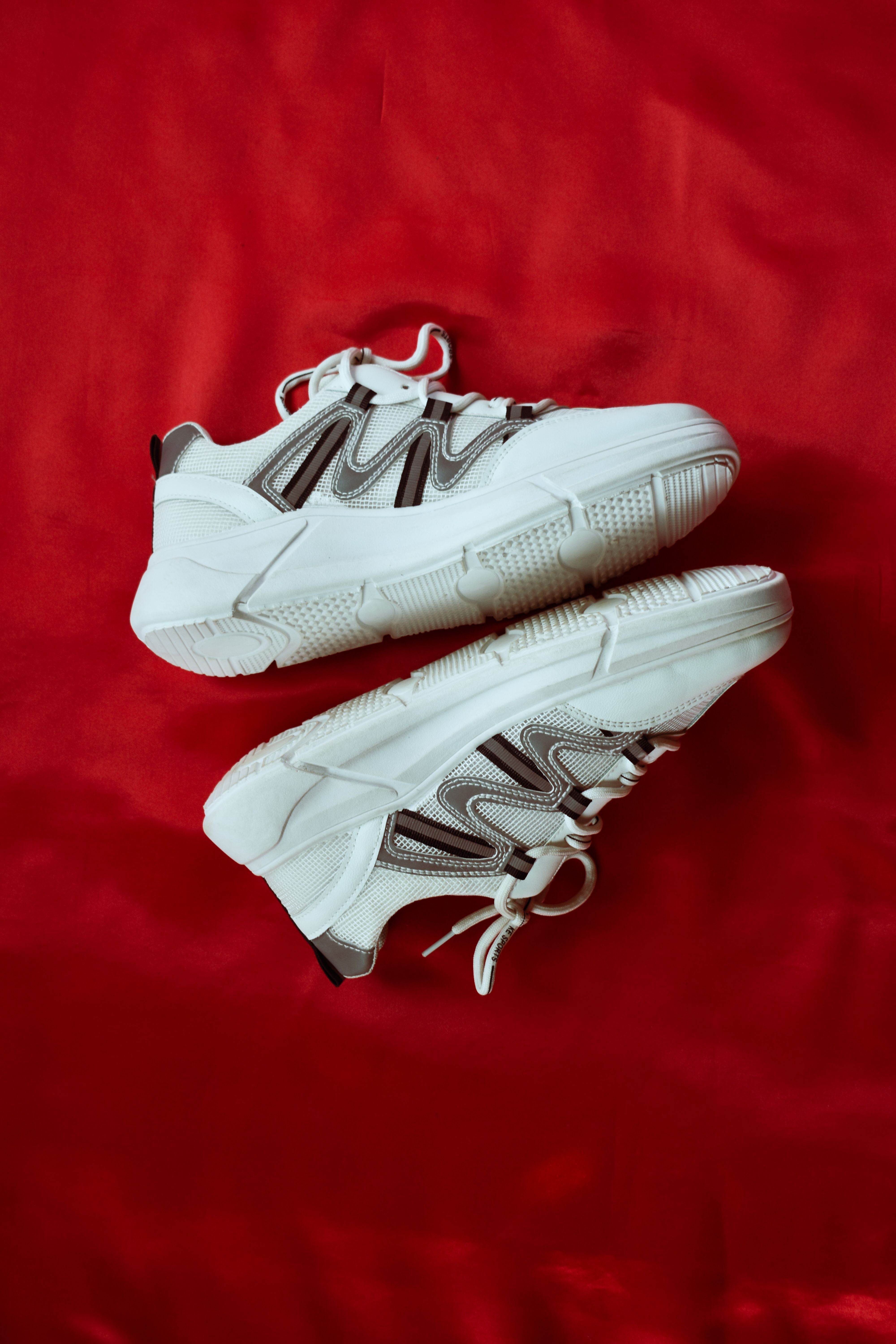 Sepasang sneakers kanvas putih di atas kain merah
