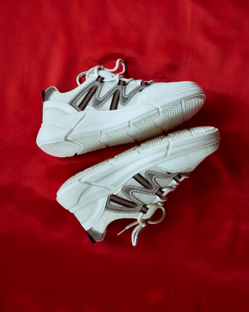 Sepasang sneakers kanvas putih di atas kain merah