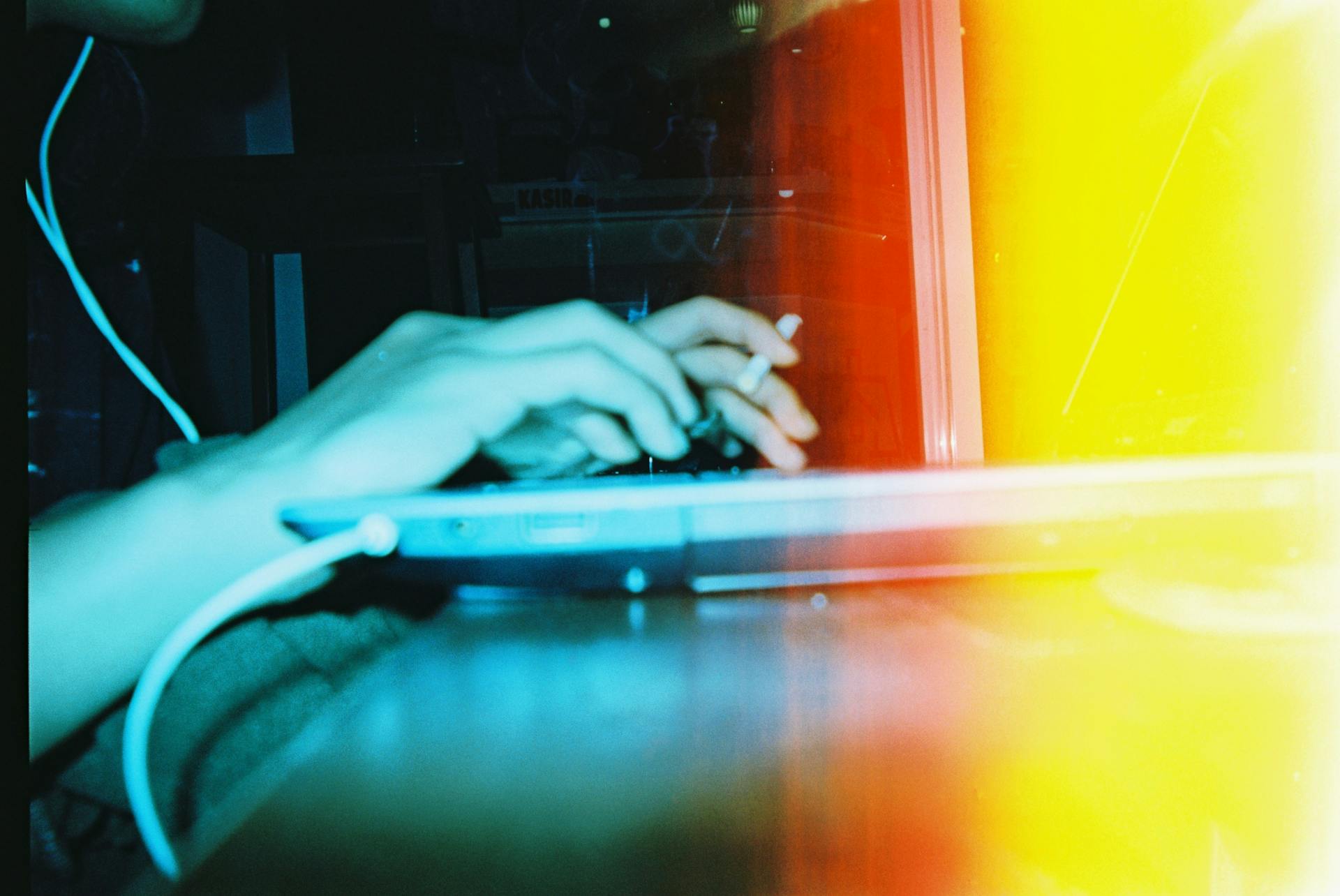 Creative photo of hands typing on a laptop with cigarette and blurred light effect.