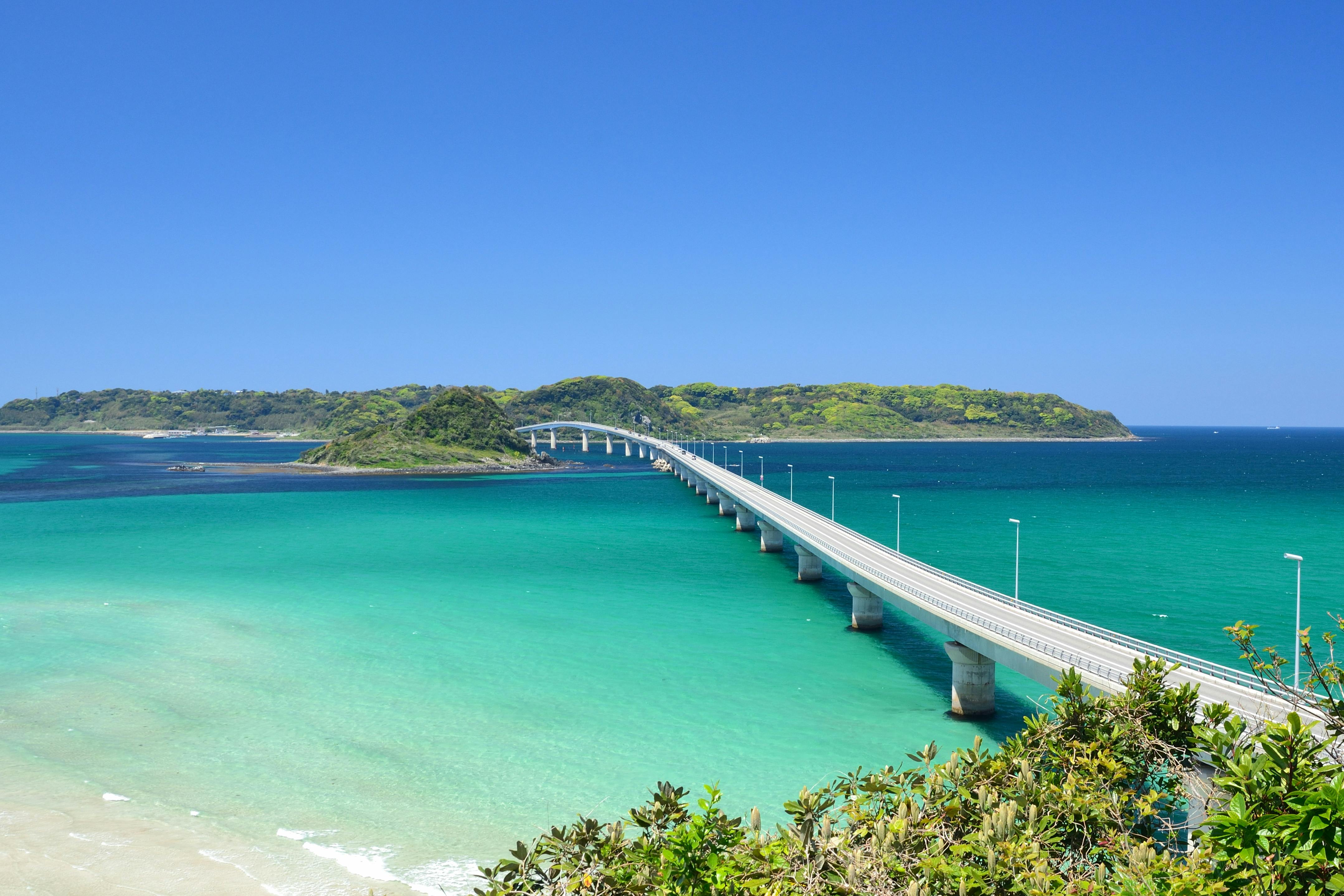 Scenic view of Tsunoshima Bridge spanning turquoise waters in Yamaguchi, Japan under a clear blue sky.