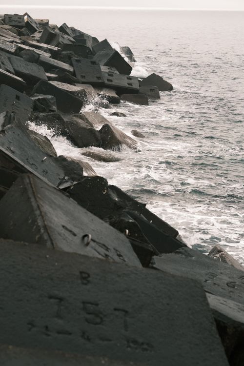 Free Waves crashing against geometric concrete breakwater blocks along the coast, showcasing ocean resilience. Stock Photo