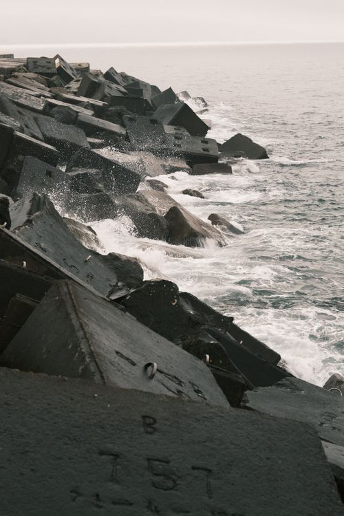 Free Waves crash against geometric concrete blocks on a coastal shoreline, showcasing rugged sea defenses. Stock Photo