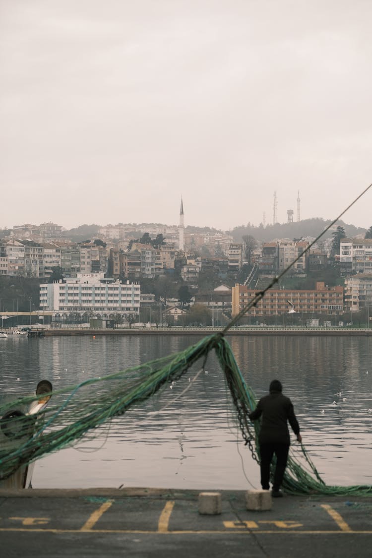 Man With Green Fishing Net And City Waterfront