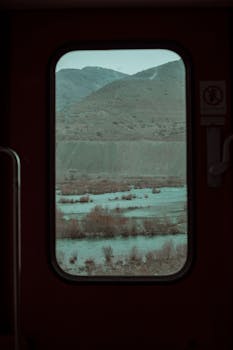 Peaceful mountain and river scene viewed through a train window.