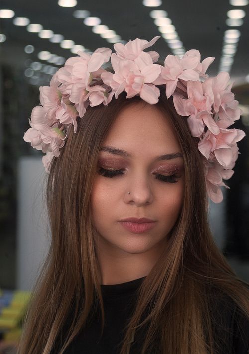 Free Close-up portrait of a young woman with a flower headband and shimmering makeup indoors. Stock Photo