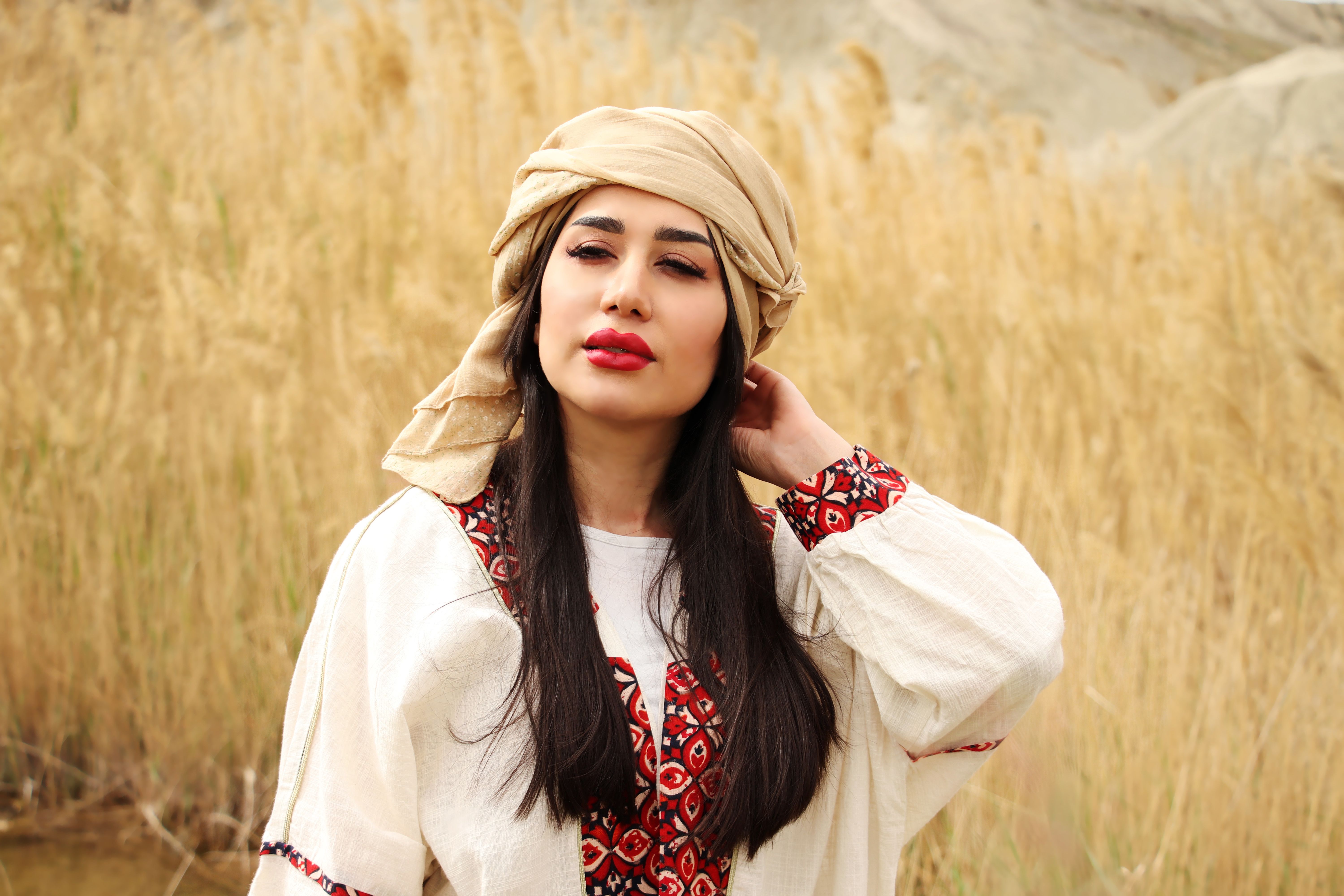 A woman in white and red floral long sleeve shirt standing on brown grass field, Comoros