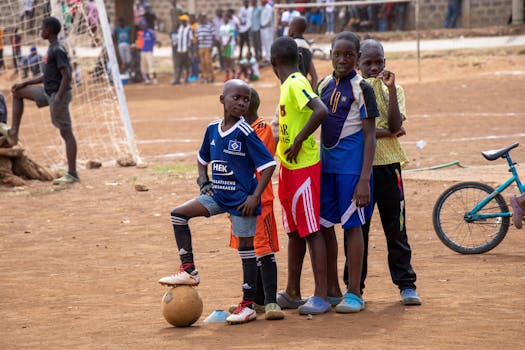Group of children having fun playing soccer outdoors on a dirt field.