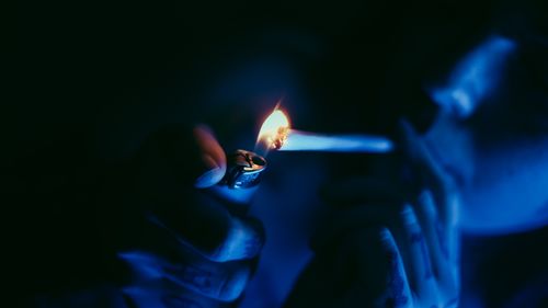 Free A close-up of hands lighting a cigarette with a blue hue, creating a moody atmosphere. Stock Photo
