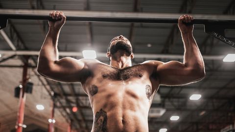 Shirtless bodybuilder showcasing strength during an intense workout on a pull-up bar in a gym.