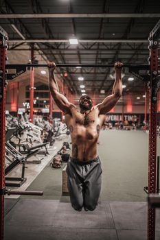 Muscular man doing pull-up exercises in a gym, showcasing strength and fitness indoors.