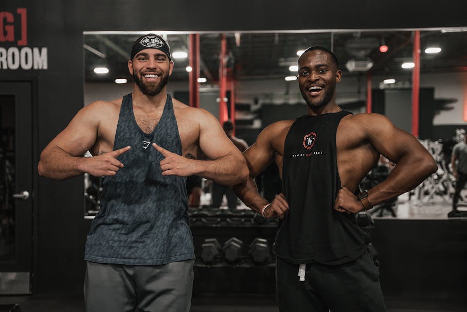 Two muscular men smiling while posing confidently in a gym environment.
