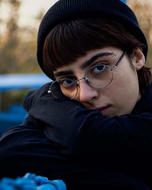 Free Close-up portrait of a woman wearing a beanie and glasses, enveloped in a reflective mood. Stock Photo