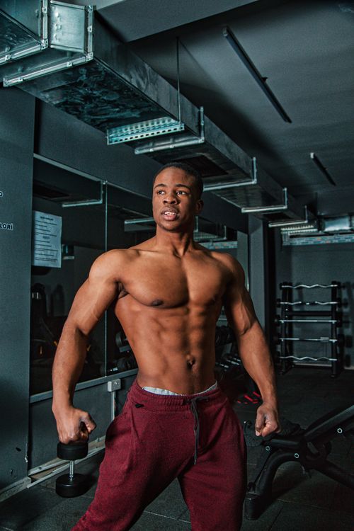 Free A fit and muscular man with a topless torso poses confidently in a gym setting. Stock Photo