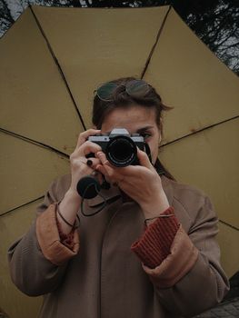 A woman holds a vintage camera under an umbrella on a cloudy day in Turkey.