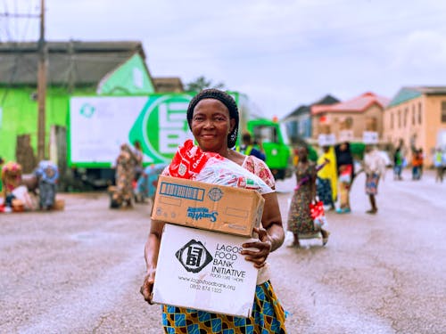 A Woman Carrying Cardboard Box while Smiling at the Camera