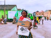 Smiling woman holding a food box from Lagos Food Bank on a busy street in Lagos, Nigeria.