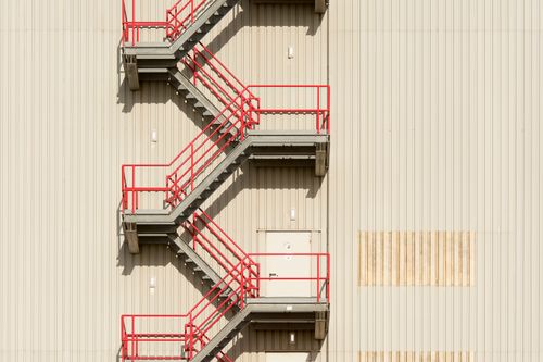 Free A minimalist exterior view of a building with a striking red staircase against a beige backdrop. Stock Photo