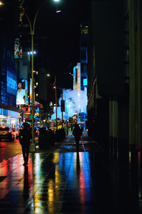 Free A lively urban street scene at night with glowing lights and wet reflections on the sidewalk. Stock Photo