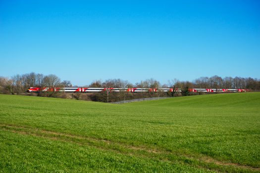 A sleek red and white train speeds through Knebworth countryside under a vibrant blue sky.