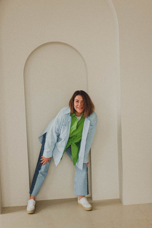 Woman Smiling in Light Blue Polo Long Sleeve Posing Against Concrete White Wall